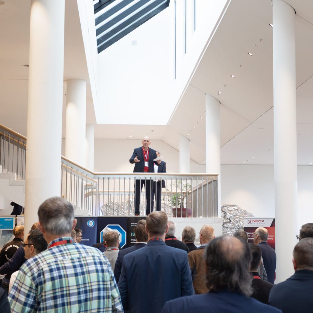 Ein Geschäftsmann spricht von einer Galerie aus zu einem Publikum bei einer Konferenz oder Messe in einem modernen Gebäude.