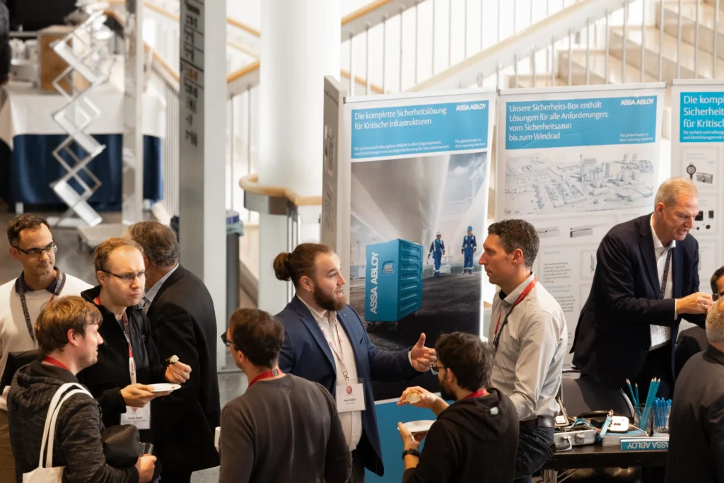 Teilnehmende tauschen sich an einem Messestand über Sicherheitslösungen für kritische Infrastrukturen aus.