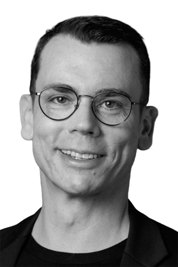 Schwarz-Weiß-Porträt eines lächelnden Mannes mit runder Brille und dunklem Haar, professionell und freundlich.