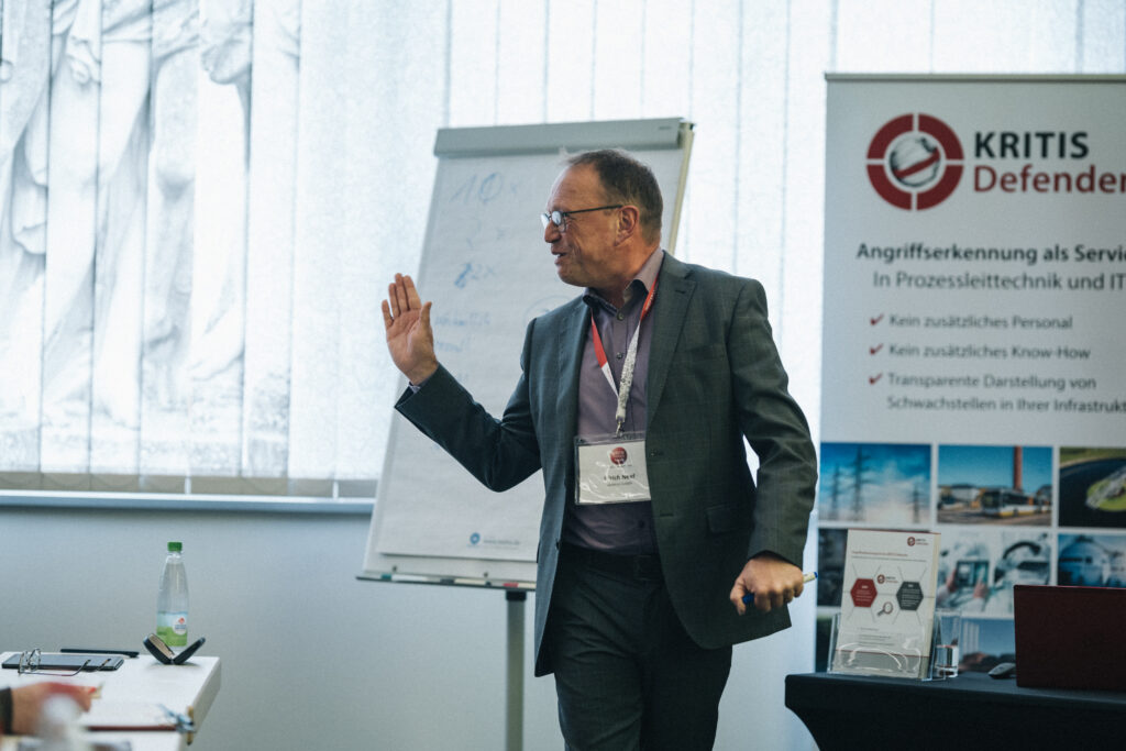 Ein Mann im Anzug präsentiert auf einer IT-Sicherheitskonferenz den KRITIS Defender Service für Angriffserkennung.