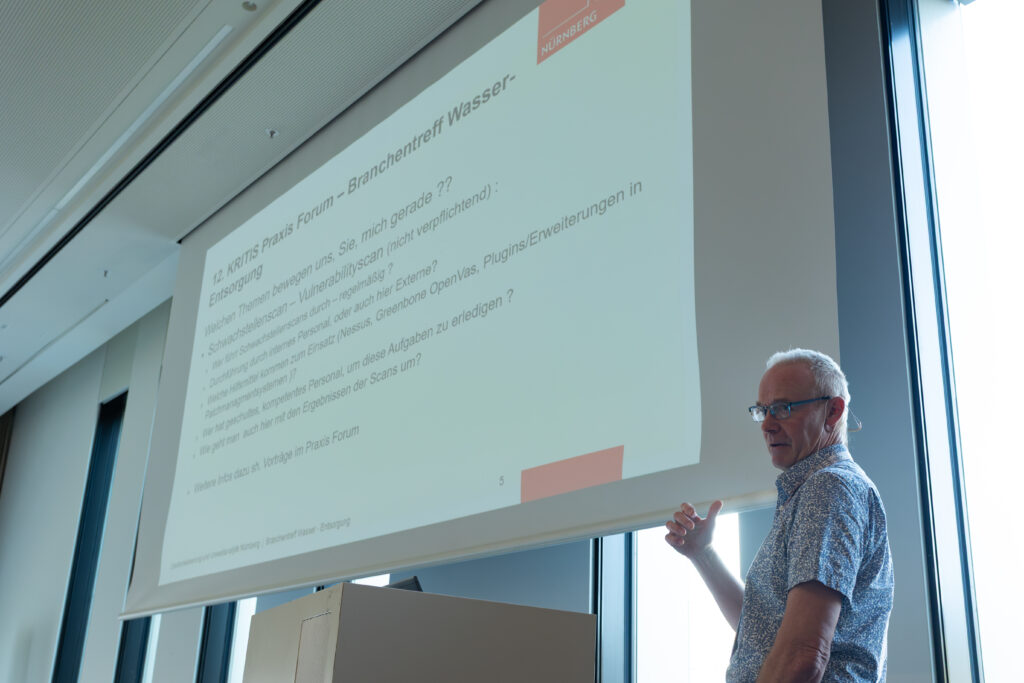 Ein Mann präsentiert auf dem KRITIS Praxis Forum zu Wassermanagement und Entsorgung, mit einer Folie über Schwachstellenscans.