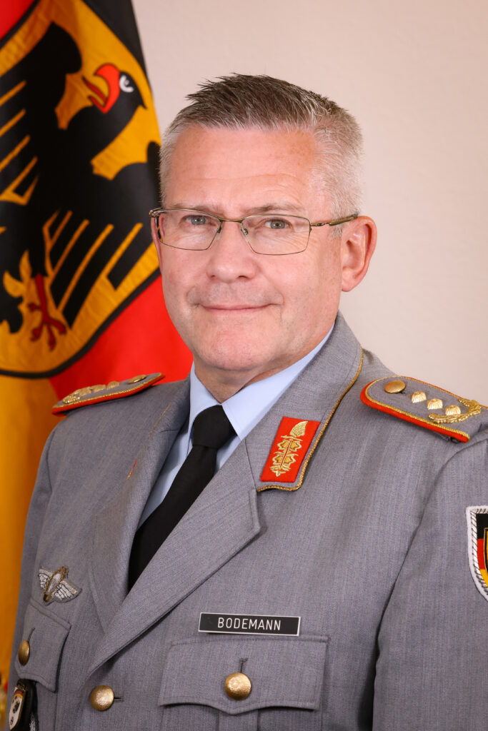 Porträt eines Offiziers in Bundeswehr-Uniform mit Namensschild 'BODEMANN' vor einer Deutschlandflagge.