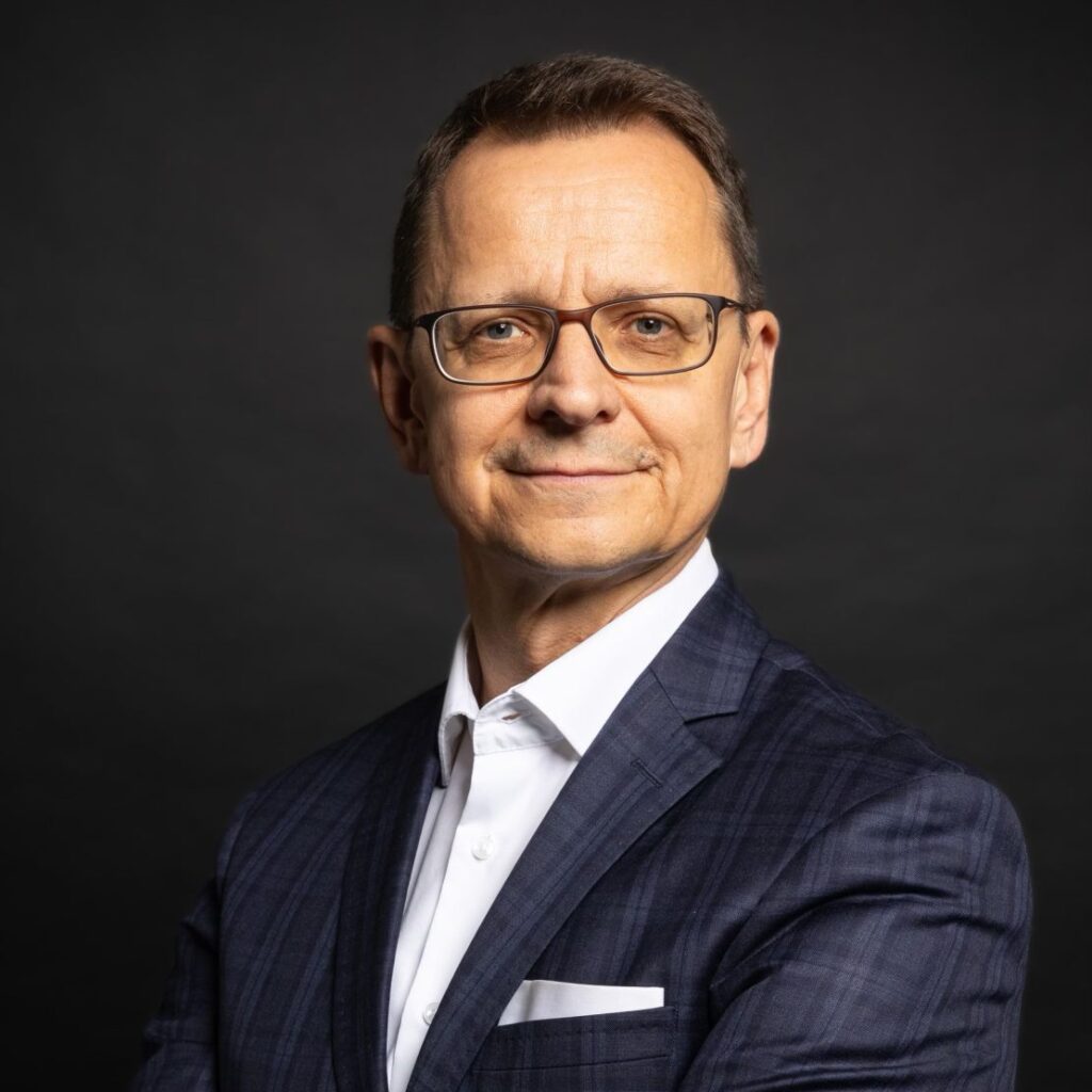 Ein Porträt eines seriösen Geschäftsmannes mittleren Alters mit Brille, dunkelblauem Anzug und verschränkten Armen.