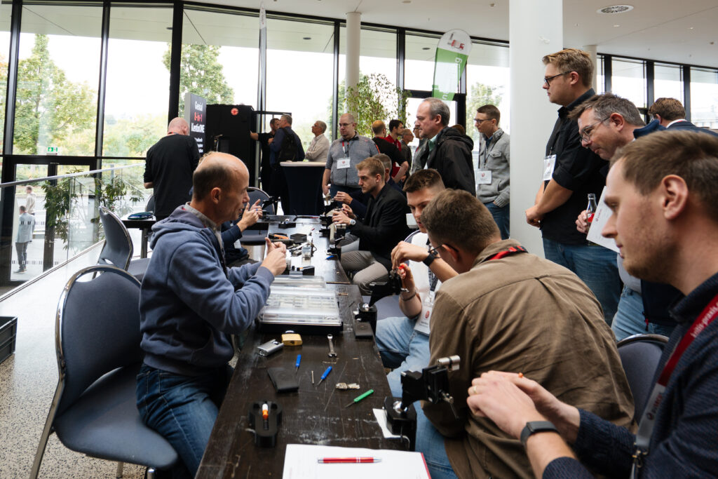 Männer nehmen an einem Workshop teil, bei dem sie Schließmechanismen und Schlösser reparieren. Sie sitzen an einem Tisch und halten Werkzeuge in der Hand.